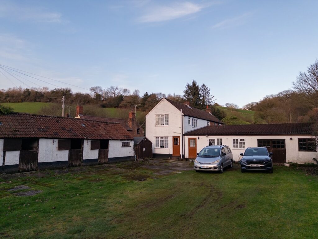 Rural farmhouse with stables and cars parked outside